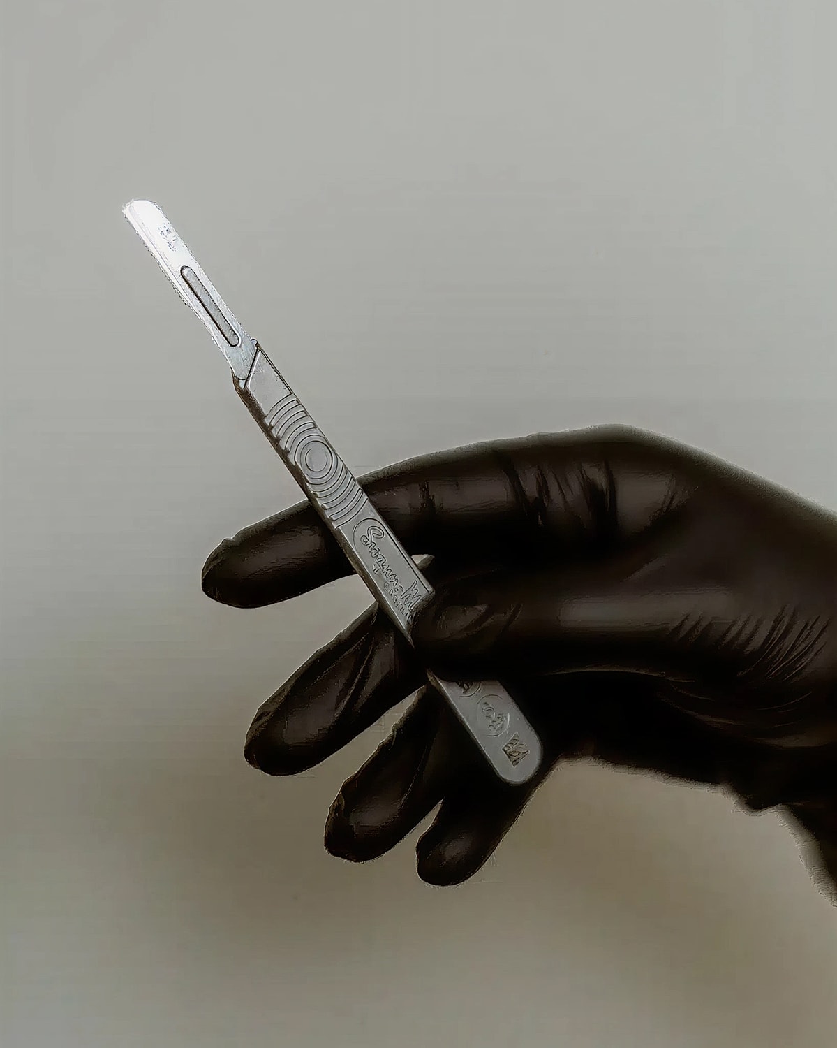 Hand holding a scalpel with black gloves.