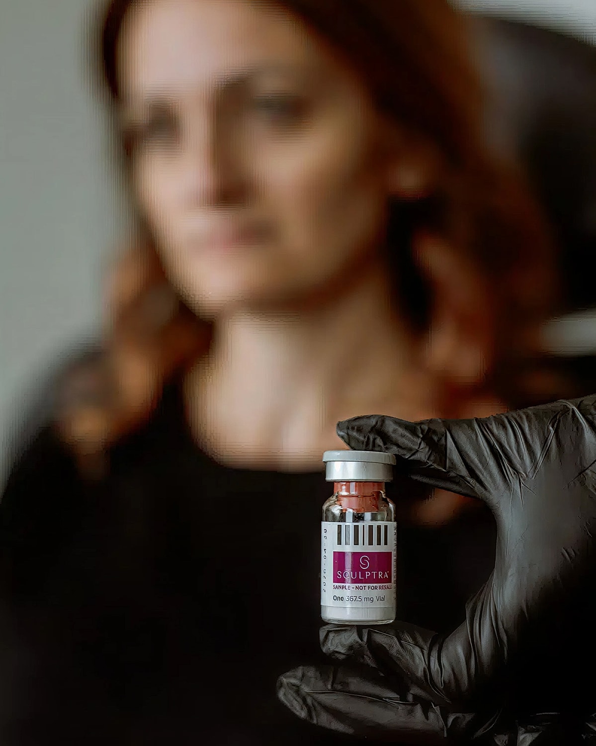 Hand holding Sculptra vial, blurred background.