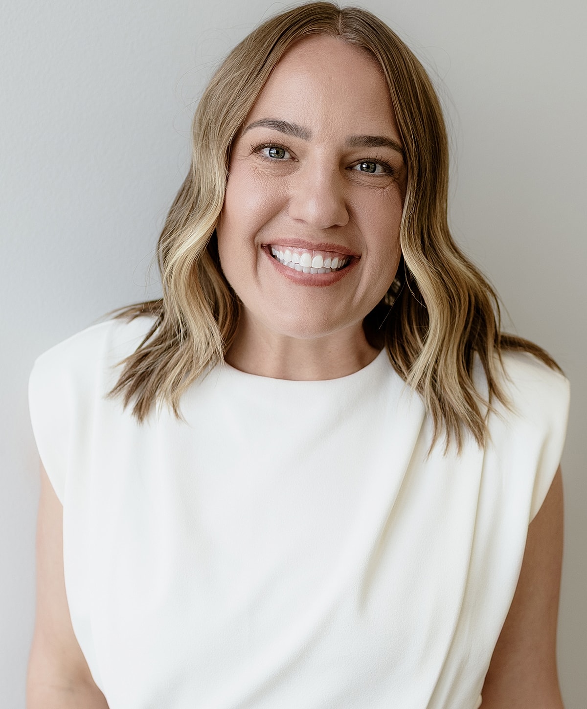 Smiling woman in casual attire against concrete wall.